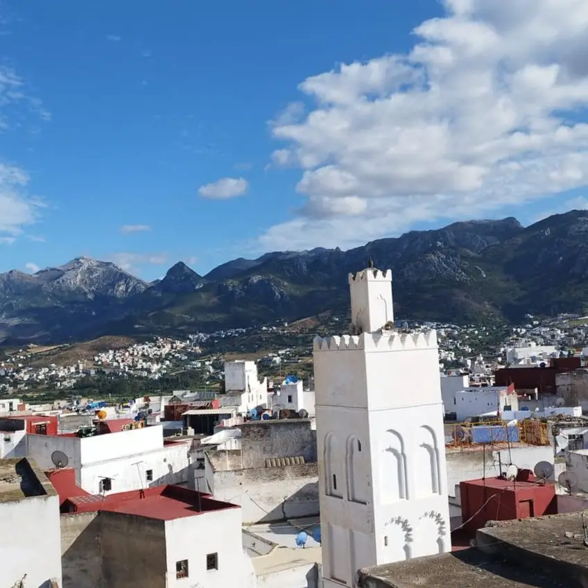 Toits blancs d’une médina et un minaret, au pied de montagnes rocheuses sous un ciel bleu